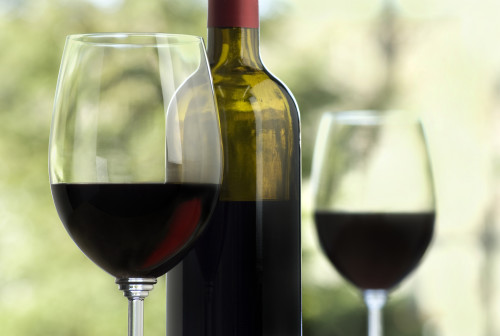 close up of wine glass, red glow visible, bottle and second glass soft focus in background, outdoors